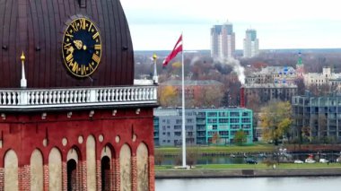 Görüntü Riga, Letonya 'nın hava manzarasını gösteriyor. Riga Katedrali saat kulesi, Letonya bayrağı, modern binalar ve sonbahar yaprakları arasında Daugava Nehri..
