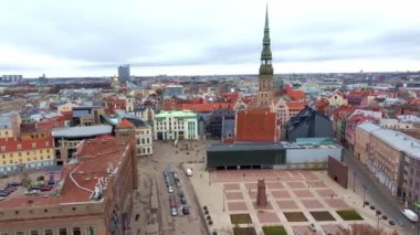 Riga, Letonya 'nın hava perspektifi, çeşitli mimari yapıların ortasında sergilenen St. Peter Kilisesi, kırmızı kiremitli çatılar ve bulutlu gökyüzü altında modern binalar.