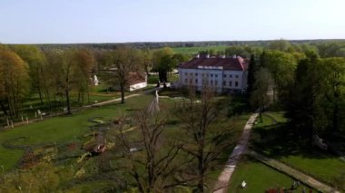 Pakruojis Malikanesi, beyaz cephesi ve kırmızı çatısı ile renkli lale yataklarıyla ve bir kaplumbağa da dahil olmak üzere tuhaf heykelleriyle çevrili..