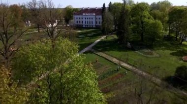 Pakruojis Malikanesi, beyaz cephesi ve kırmızı çatısı ile renkli lale yataklarıyla ve bir kaplumbağa da dahil olmak üzere tuhaf heykelleriyle çevrili..