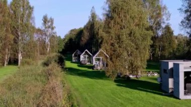 Büyük cam pencereli çağdaş yazlık evler uzun ağaçların arasına kurulmuştur. Bisikletler yakınlarda park halinde, açık hava aktiviteleri için fırsatlar var..