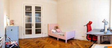 A minimalist room features a pink bed with patterned pillows, a modern desk with a red chair, and natural light streaming through double glass doors. clipart