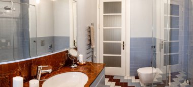 Çağdaş banyo açık mavi metro fayansları, yuvarlak lavabolu kahverengi mermer tezgah ve kapalı bir duş içerir. Döşeme kiremitleri dekora uyuyor.