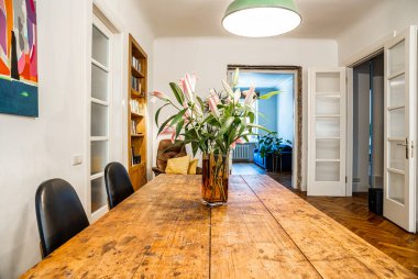 Pembe çiçekli kırsal ahşap bir yemek masası yukarıdaki bir lambayla aydınlatılır. Modern sanat duvarları süslüyor ve bir kitaplık boşluğa sıcaklık katıyor..