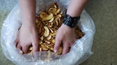 Bir çift el, kırmızı kabuklu ince kesilmiş elma dilimleri ve temiz bir plastik torbadan kepçelenmiş altın kahverengi bir renk tutar. Sol bileğinde siyah bir saat var..