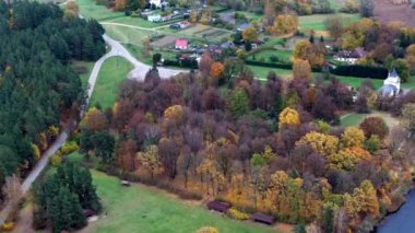 Hava perspektifi, sonbahar ağaçlarıyla çevrili bir kırsal köyü yakalar. Dönek bir yol, canlı sonbahar renklerini gösteren tarlalar ve ormanlardan geçer..
