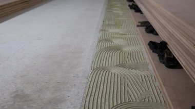 Alt kattaki dalgalı desenlere uygulanan yapıştırıcının detaylı görünümü, zemin tahtaları sıralanmış ve kapalı bina inşaatında güvenli bir şekilde klemplenmiş.