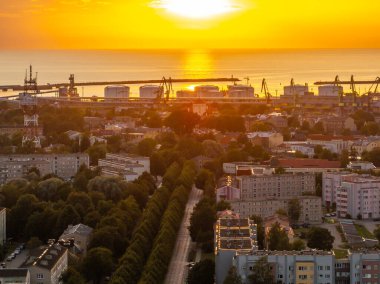 Günbatımı Letonya 'nın Ventspils kentinin üzerinde altın bir parıltı yayarken, depolama tankları ve vinçlerle liman tesislerinin yanı sıra konut binaları ve ağaçlarla kaplı caddeler de de üzerinde parlıyor..