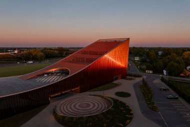 Letonya 'daki Ventspils Konser Salonu Latvija, yollar, ağaçlar ve uzak yapılarla çevrili canlı kırmızı bir dış ve açısal tasarıma sahiptir..