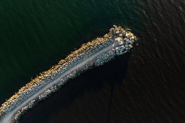 Etrafındaki derin sularla çelişen, uçlarında büyük kayalar ve beton bloklar olan uzun bir iskeleden oluşan havadan bir perspektif..