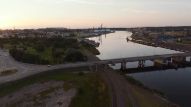 Ventspils, Letonya, nehir, köprü, döner kavşak ve demiryolu manzarası. Endüstriyel binalar ve turnalar berrak bir gökyüzünün altında görülebilir..