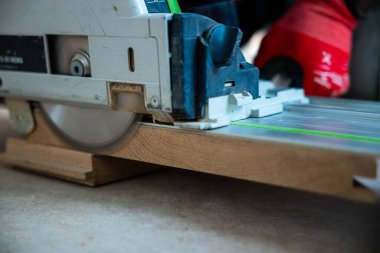 Kırmızı eldivenli biri tarafından işletilen yuvarlak bir testere kılavuz korkulukta tahtayı keser. Odak noktası bıçağın hassasiyeti ve ahşap işçiliğinin dinamik hareketi..