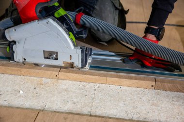 Kişi ahşap kalasları kesmek için kılavuz korkuluklu dairesel testere kullanır. Kırmızı eldivenler ve elektrikli hortum profesyonel bir atölye ayarlarını gösteriyor..