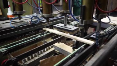 Metal kolları, hortumları ve kabloları olan otomatikleştirilmiş bir fabrika kurulumu. Ahşap bir parça üretim hattında işleniyor..