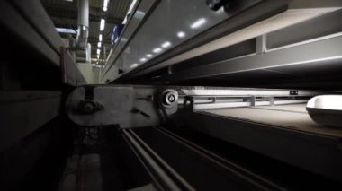 Görünür borular ve yapılarla loş ışıklandırılmış endüstriyel bir ortamda metal zincir sürücüsü ve taşıyıcı sistem de dahil olmak üzere makine bileşenlerinin ayrıntılı görünümü.