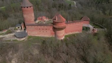 Ortaçağ kırmızı tuğlalı kalesinde birden fazla kule, silindirik bir kule, dik kiremitli çatılar ve orman alanlarıyla çevrili görünür kalıntılar var..
