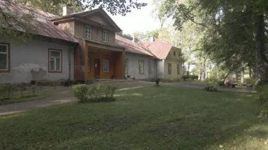 İçinde yıpranmış metal çatı, ahşap ve tuğla elementler, birden fazla pencere ve olgun ağaçlar ve saksı bitkileri olan çimenli bir bahçe bulunan eski bir bina..