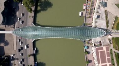 Gürcistan 'ın Tiflis kentindeki Barış Köprüsü' nün cam ve çelik tepe örtüsü, şehir sokakları, geometrik bahçeler ve aşağıdaki Kura Nehri 'nin manzarası..