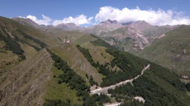 Gergeti Trinity Kilisesi, Gürcistan 'ın Stepantsminda yakınlarındaki bir tepenin tepesinde, dağ sıraları ve ormanlarla çevrili, Kazbek Dağı ise kısmen bulutlu..