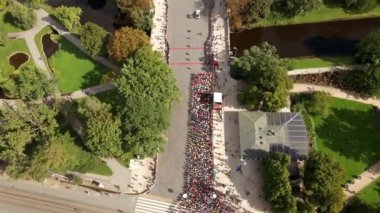Riga, Letonya 'daki bir maratonun hava görüntüsü, kırmızı çizgiler, yakındaki park alanları, ağaçlar, patikalar ve yeşil çatılı bir binada katılımcıları gösteriyor..