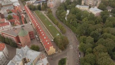 Riga, Letonya 'da bir maratonun hava perspektifi, kıvrımlı bir yolda koşucuların bulunduğu, park, kanal ve kırmızı çatılı tarihi binalarla çevrili..