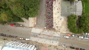 Riga, Letonya 'da geniş bir yolda, tramvay rayları, park edilmiş arabalar ve manzaralı yeşil çatılı bir binada büyük bir kalabalık maratona katılıyor..