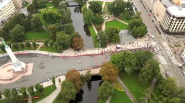Riga, Letonya 'daki bir maratonun hava görüntüsü, kontrol noktası yakınlarındaki katılımcılar, kırmızı engeller, park yolları, ağaçlar, su ve kentsel caddeler.