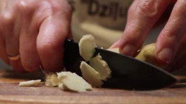 Eller taze zencefil kökünü ince ince keser, hatta tahta kesme tahtasındaki parçaları bile siyah bir bıçakla. Kök ve bıçağın dokusu görülebilir..