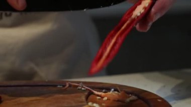 Eller kırmızı biberi dilimlemek için keskin bir bıçak kullanır. Tahta kesme tahtasının üzerinden çekirdekleri çıkarır. Canlı renkler ve dokular odaklı.