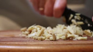 Eller, ahşap kesme tahtasındaki açık renkli yiyecekleri ince ince doğramak için siyah bıçak kullanır..