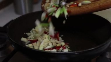Taze soğan, sarımsak ve kırmızı biber, ahşap bir kesme tahtasından yağlı siyah bir tavaya taşınır..