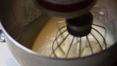 Kablo çırpıcılı bir karıştırıcı pürüzsüz, paslanmaz çelik bir kasede hafif bir hamuru karıştırır. Vurucu tortusu aktif hazırlığı vurguluyor.