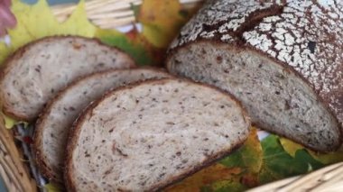 Bir el dokuma sepetinde, canlı sarı ve yeşil sonbahar yapraklarıyla süslenmiş, mevsimsel hazırlıkları vurgulayan rustik çoklu tahıllı ekmek dilimlerini tutuyor..