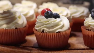 Çilek ve yaban mersiniyle kaplı, turuncu kaplamalı kekler, arka planda bulanıklık olan ahşap bir yüzeye yerleştirilmiş..