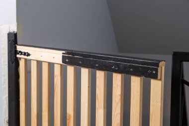 Duvarla metal parmaklıklar arasına gri eğimli tavanın yanına kurulmuş dikey levhaları ve siyah metal donanımlı kapalı ahşap kapı..