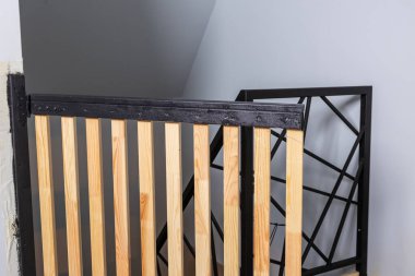 Açık renkli tahta çıtçıtalar ve kapalı bir alanda siyah metal üst korkuluklar. Geometrik bir siyah metal çerçeve açık gri bir duvara dayanır..