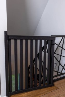 Dikey kirişleri ve mandal mekanizması olan siyah metal bir güvenlik kapısı merdivenin tepesinde duruyor. Ahşap döşeme ve tarafsız duvarlar iç kısmı tamamlıyor..