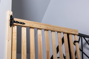 Kapalı ahşap kapı dikey levhalar ve siyah metal donanımla, açık gri duvarlı ve minimal dizaynlı bir merdivenin tepesine yerleştirilmiş..