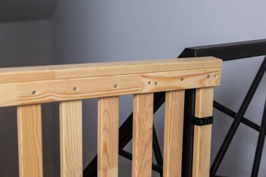 Çapraz dizaynlı siyah metal korkuluklara sade gri duvarlara dayanan tahta güvenlik kapısı..