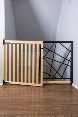 Dikey tahta çıtçıtlı ve geometrik siyah metal dizaynlı bir güvenlik kapısı, merdivenin tepesine yerleştirilmiş. Ahşap döşemeli açık gri bir duvara yaslan..