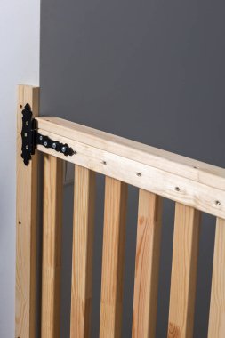 Dikey çıta ve dekoratif siyah metal menteşeli ahşap bir kapı. Kapalı bir ortamda düz gri bir duvara dayanıyor..