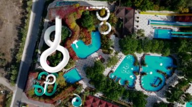 Dolambaçlı slaytların, eşsiz şekilli havuzların ve gevşeme alanları olan yemyeşil bitkilerin yer aldığı hareketli bir su parkının hava perspektifi.