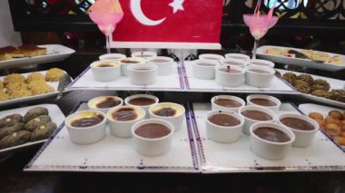 Türk bayrağının arka planına yerleştirilen ve aralarında tatlılar, kurabiyeler ve hamur işlerinin de yer aldığı beyaz ramekinlerdeki Türk tatlılarının bir seçimi.