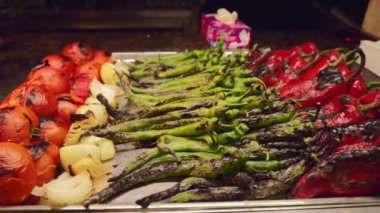 Kavrulmuş domates, soğan ve renkli biberler de dahil olmak üzere canlı bir sebze çeşidi yakınlardaki bir mendil kutusuyla metal bir tepside sergileniyor..