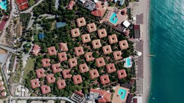 Şebeke desenli kırmızı kiremitli çatıları, güneşli havuzlu kumlu plajları ve eşsiz şekilli yüzme havuzları olan bir sahil beldesinin havadan bakış açısı..