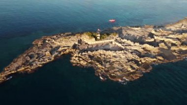 Arka planda deniz bulunan kayalık bir kıyı bölgesinde bir Türk bayrağı duruyor. Altın saat aydınlatması engebeli arazinin renklerini ve dokusunu güçlendirir..