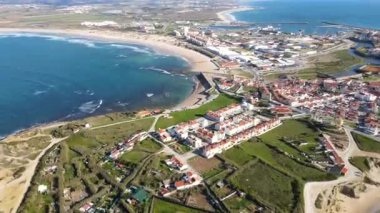 Peniche, Portekiz 'in hava perspektifi, kıyı şeridini, limanı, kırmızı çatılı beyaz binaları, kumlu plajları ve uzak rüzgar türbinlerini vurguluyor.
