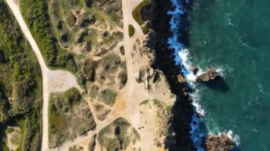 Portekiz 'in kıyı şeridine ait hava perspektifi, kayalık uçurumlar, çarpan dalgalar ve Atlantik Okyanusu boyunca uzanan bitki örtüsü bölgelerinin ortasındaki yollar..