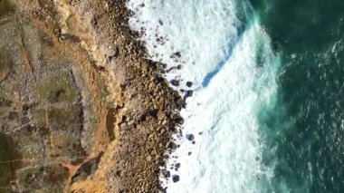 Portekiz 'in engebeli uçurumları, çimenleri ve Atlantik Okyanusu kıyılarına çarpan dalgalarla dolu kıyı şeridine dramatik bir hava perspektifi..