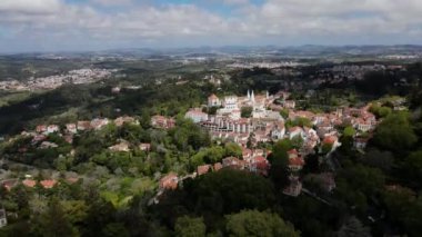 Palacio Nacional de Sintra 'nın ikiz bacaları kırmızı çatılı binalar arasında yeşil tepelere ve bulutlu gökyüzünün altındaki uzak dağlara kurulmuş..
